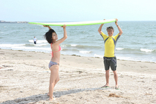 砂浜にて仲良く(?)サーフボードを担ぐ国沢光宏氏と柏木美里さん