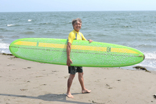 サーフボードを担ぐ国沢光宏氏、180cmの大きな身体でサーフボードもちょっと小さく見えるかも?