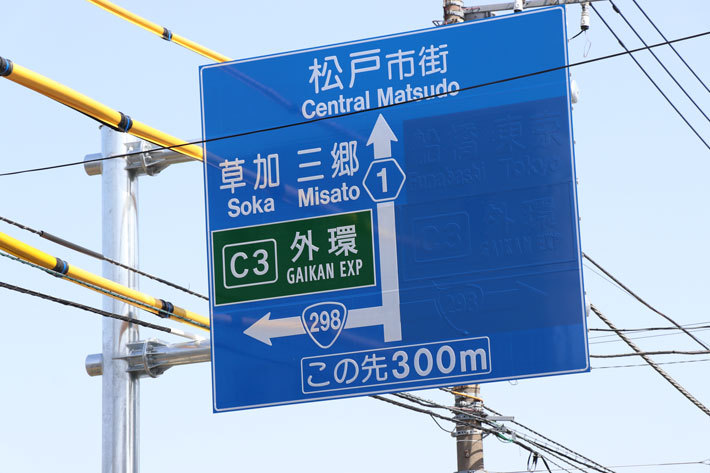 外環道・国道298号線と交差する千葉県道1号市川松戸線の看板。右方向、6月2日開通に向け準備が進む。青いシールの下にうっすら船橋・東京の文字が浮かび上がる[2018年5月15日(火)／東京外かく環状道路(外環道：三郷南IC～高谷JCT間：2018年6月2日開通予定) 報道陣向け現場公開]