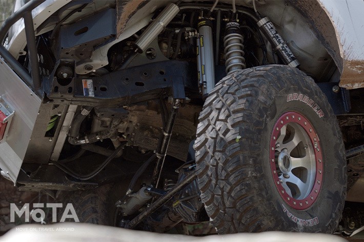 凹凸の多いオフロードをがっちりと掴むための大径タイヤの直径は怒涛の37インチ！（約94cm）まさしくNVカーゴXを象徴するポイントだ。  フロントの足回りはオフロードスペシャルとしてカスタムされ、リアは耐久性の高さを考慮してNV2500HDのリーフスプリング式を継承。凹凸路面で車体が斜めになろうが、豊かなストロークとしなやかな足回りで悪路を走り抜ける。