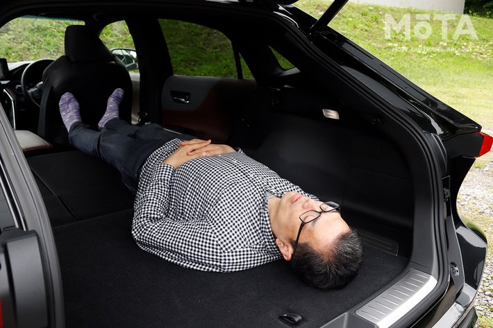 トヨタ 新型ハリアー ラゲッジ（荷室）での車中泊（イメージ）／写真ではわからないが、足元は浮いている状態。こっち向きで寝るのも良いが、テールゲートを閉じた状態にするとかなりの閉所感・圧迫感がある。[モデルの身長180cm]