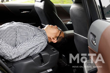 トヨタ 新型ハリアー ラゲッジ（荷室）での車中泊（イメージ）／荷室長は1805mmだが、実際には後席シート背もたれが短く頭もはみ出てしまう。この状態ではねることが出来ないから、空いている空間に荷物などを積み込み、さらにアウトドア用の就寝マットなどを用意する必要がある。[モデルの身長180cm]