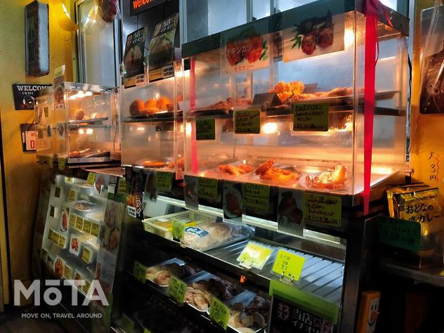 石渡チキンストアーのショーケースには焼鳥、ローストチキン、モツ煮、唐揚げなどなど、様々な総菜が並べられている。お店の中では昼夜問わず沢山のスタッフが忙しそうに調理を続けている。